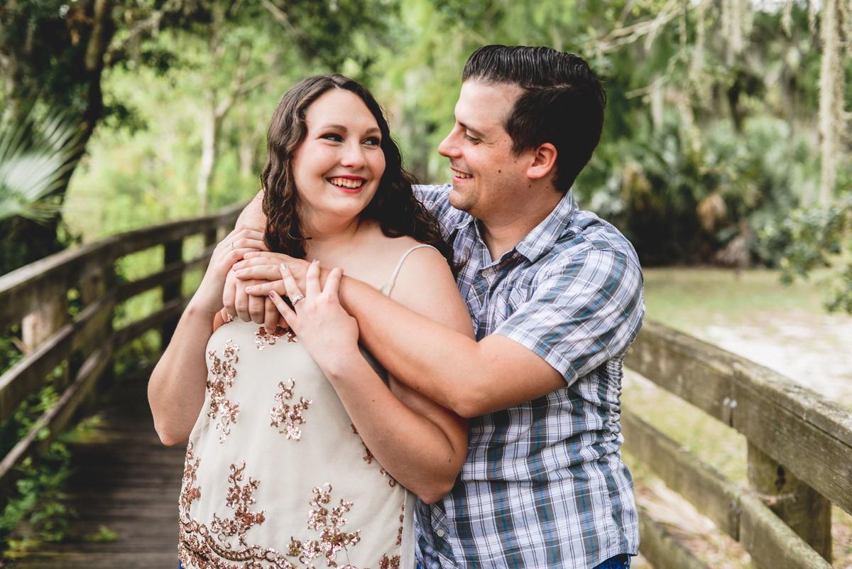 fiance, hugging, smiling, boardwalk, park, trees, moss