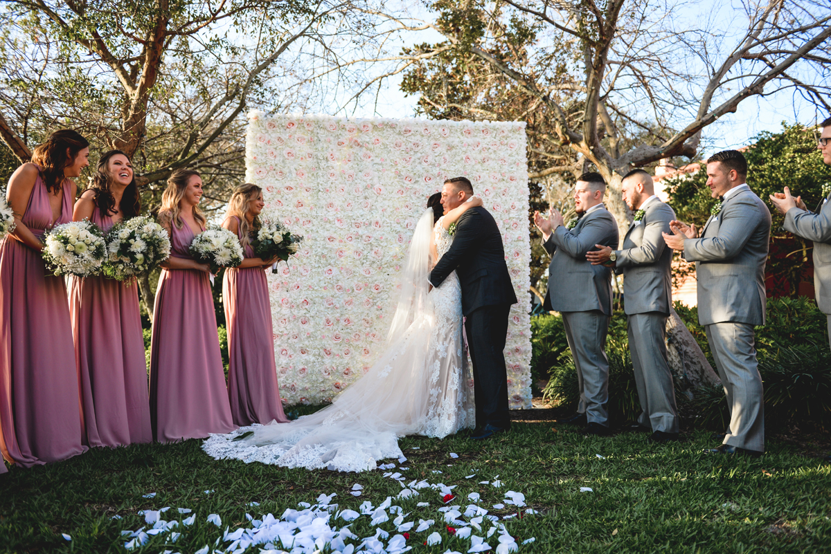 wedding, bride, groom, flower wall, grass, hugging