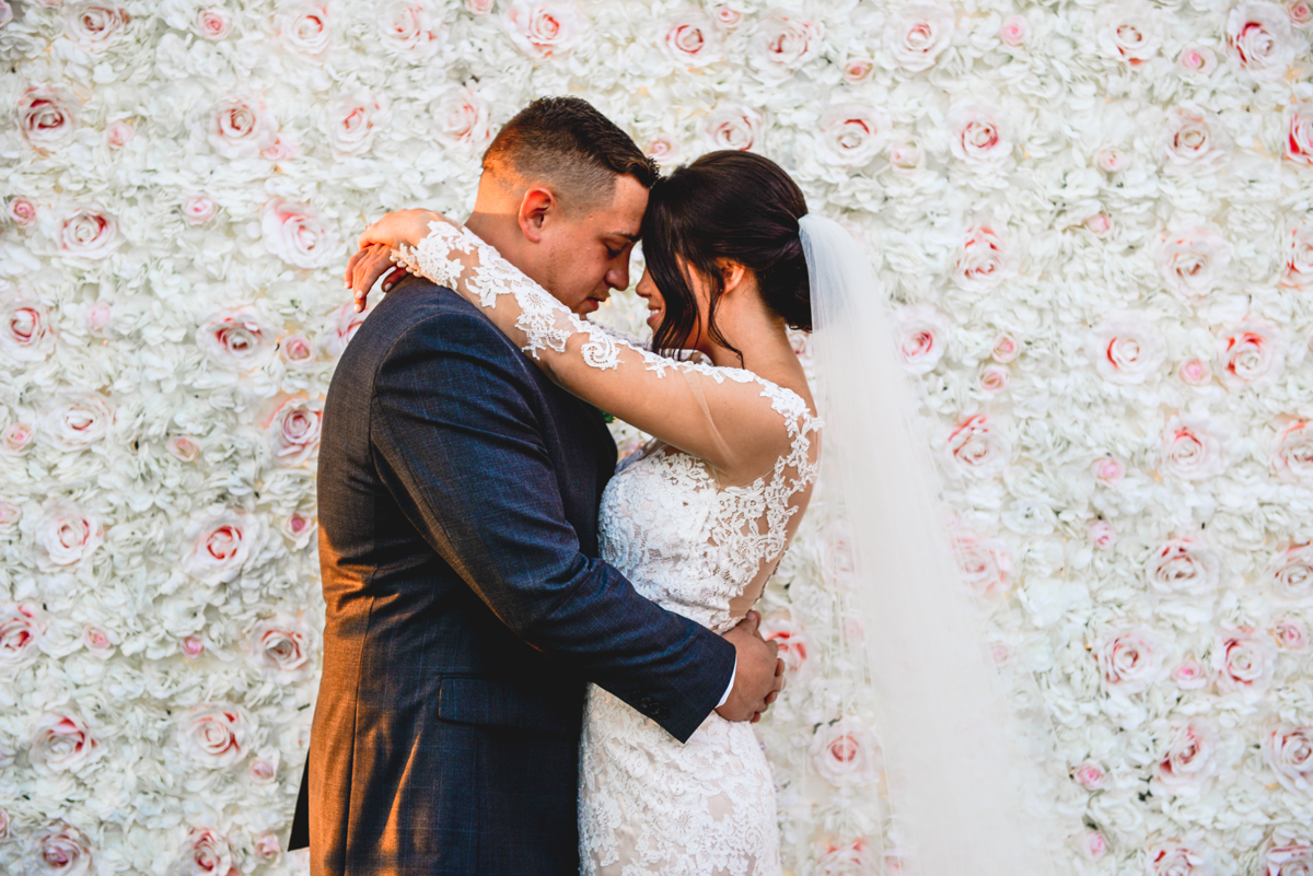 flower wall, just married, hugging, veil, wedding dress